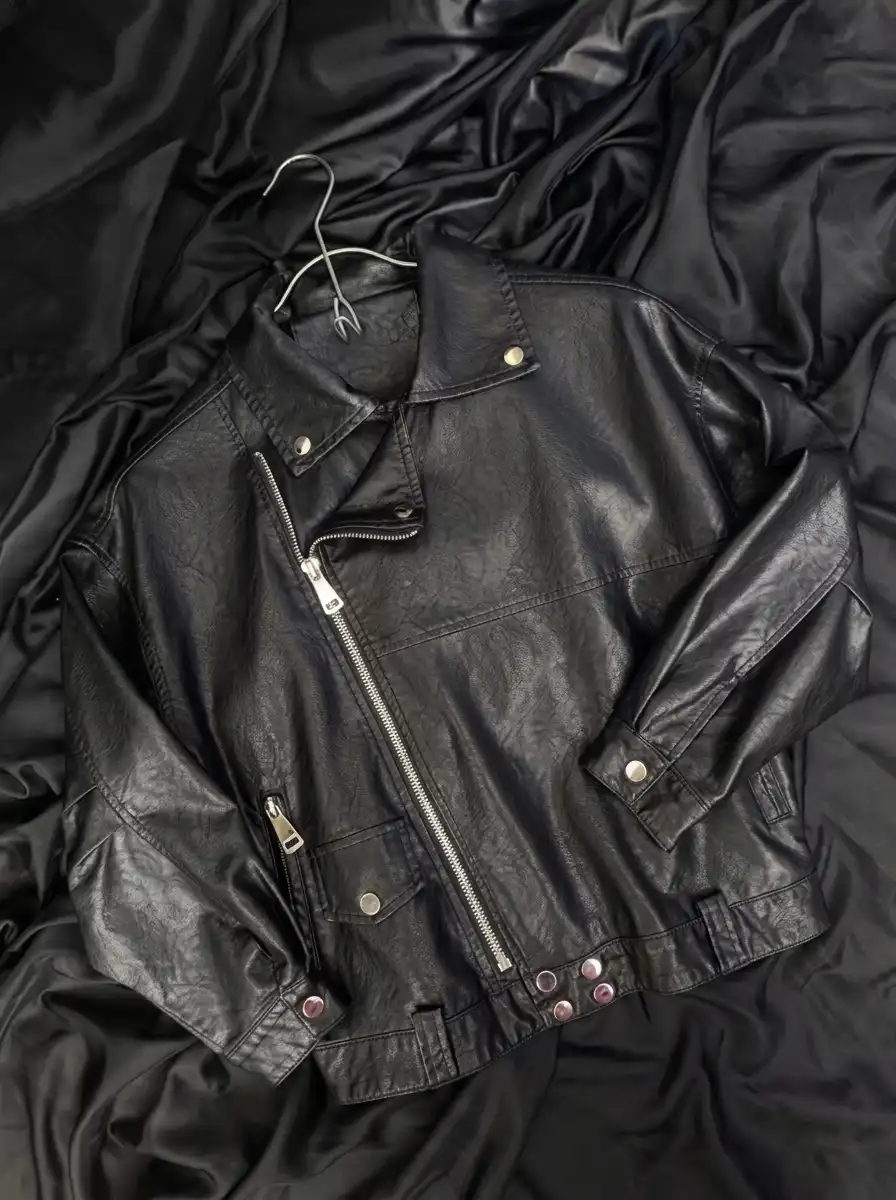 A black leather jacket laid flat, showing its smooth, light-catching surface texture.