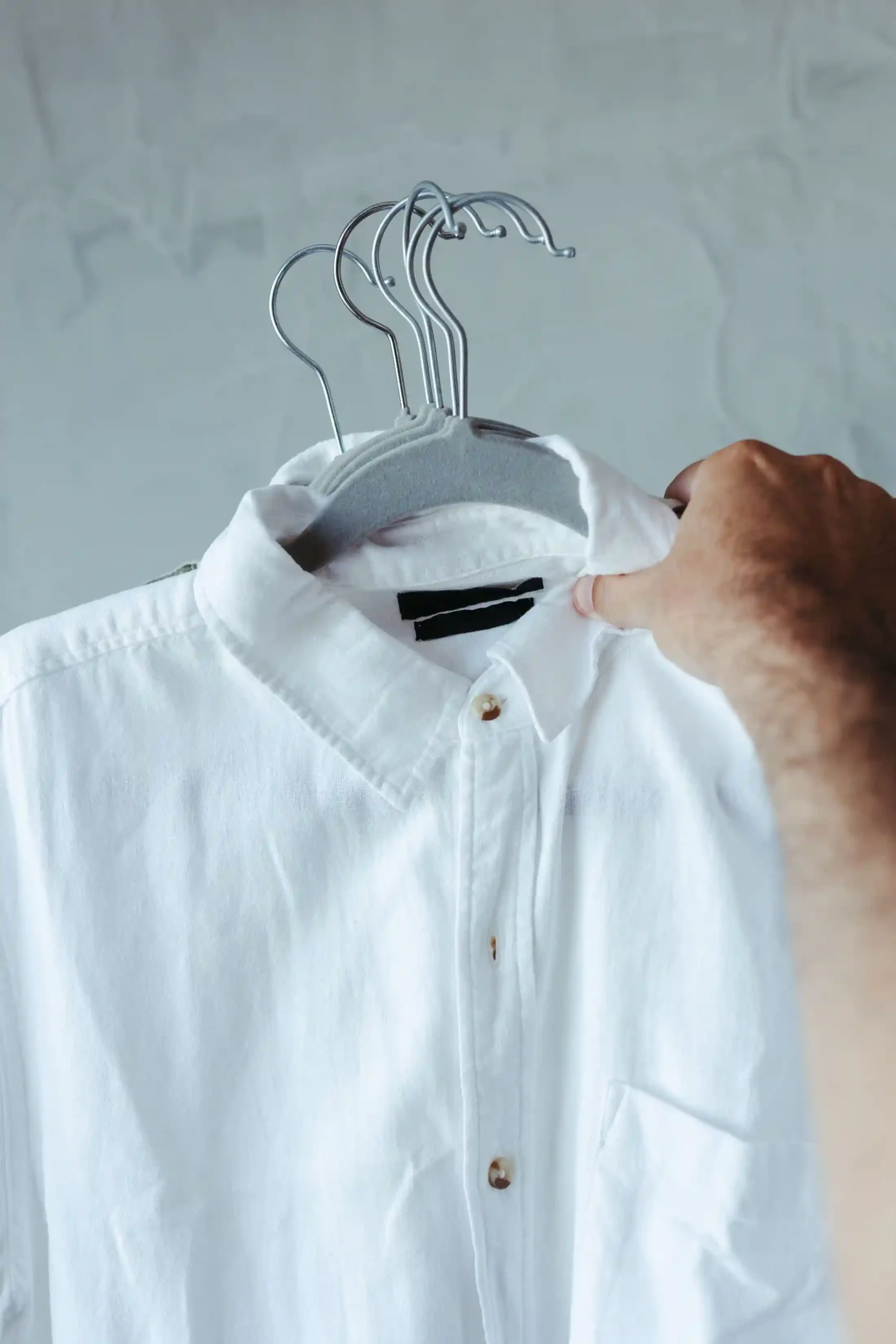 A crisp white cotton poplin button-down shirt on a wooden hanger against a plain wall.
Source type: Real photo, licensed stock marketplace.