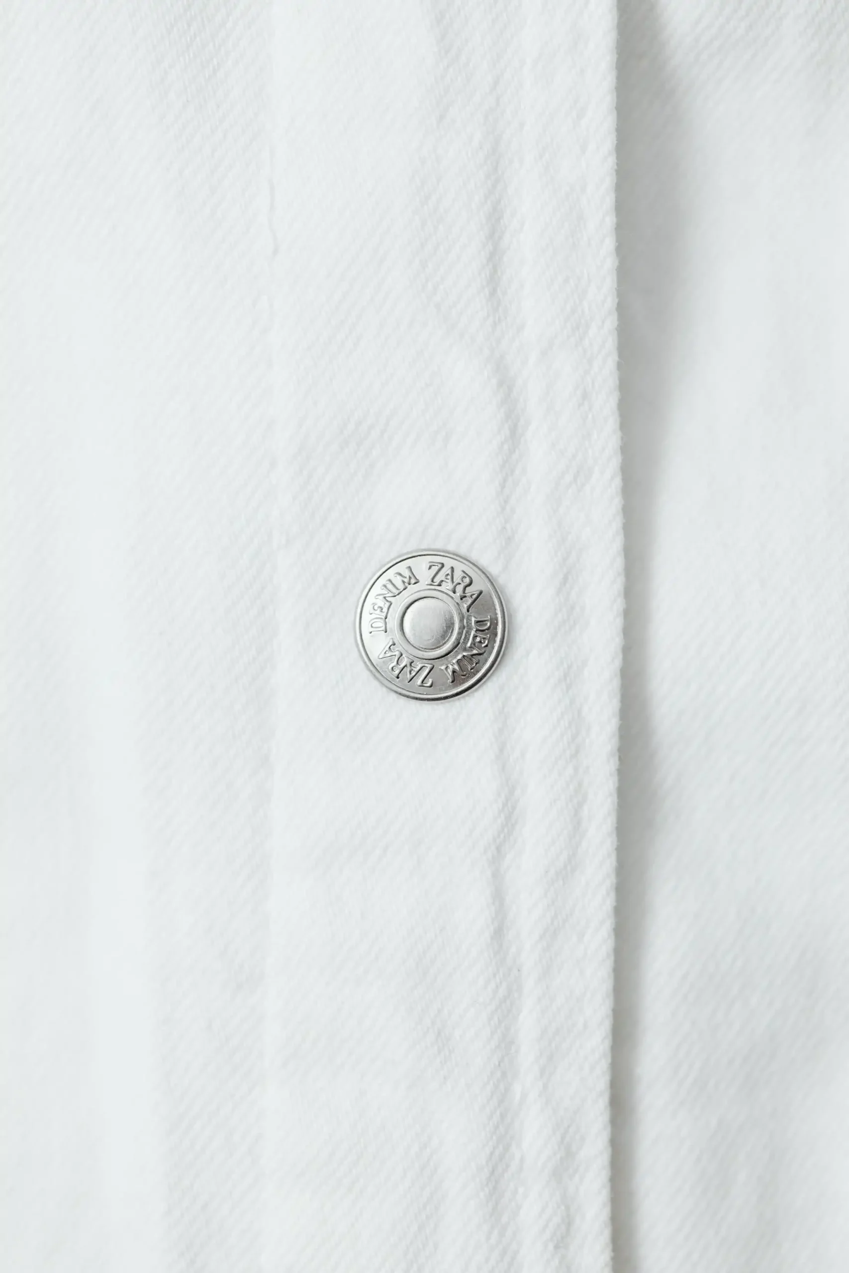 Close-up of a crisp white cotton poplin shirt showing the fine plain weave and chest pocket.