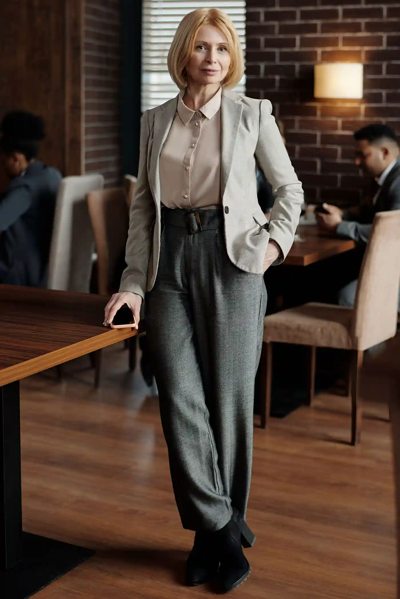 A professional woman wearing a structured blazer over a fine-gauge knit and tailored trousers in a modern sunlit office.