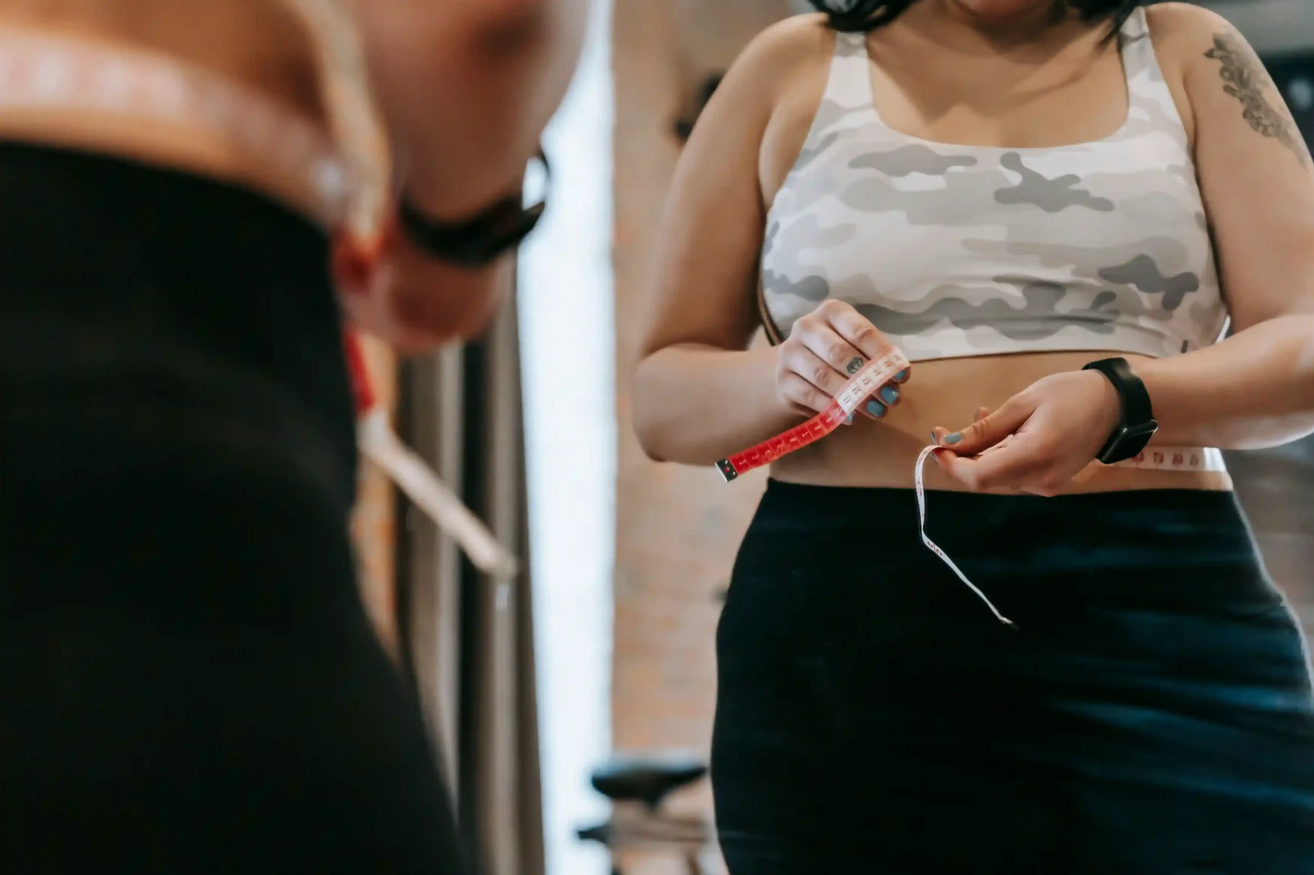 Woman checking a soft measuring tape in a mirror while taking her waist measurement.
Type: Real photo.
