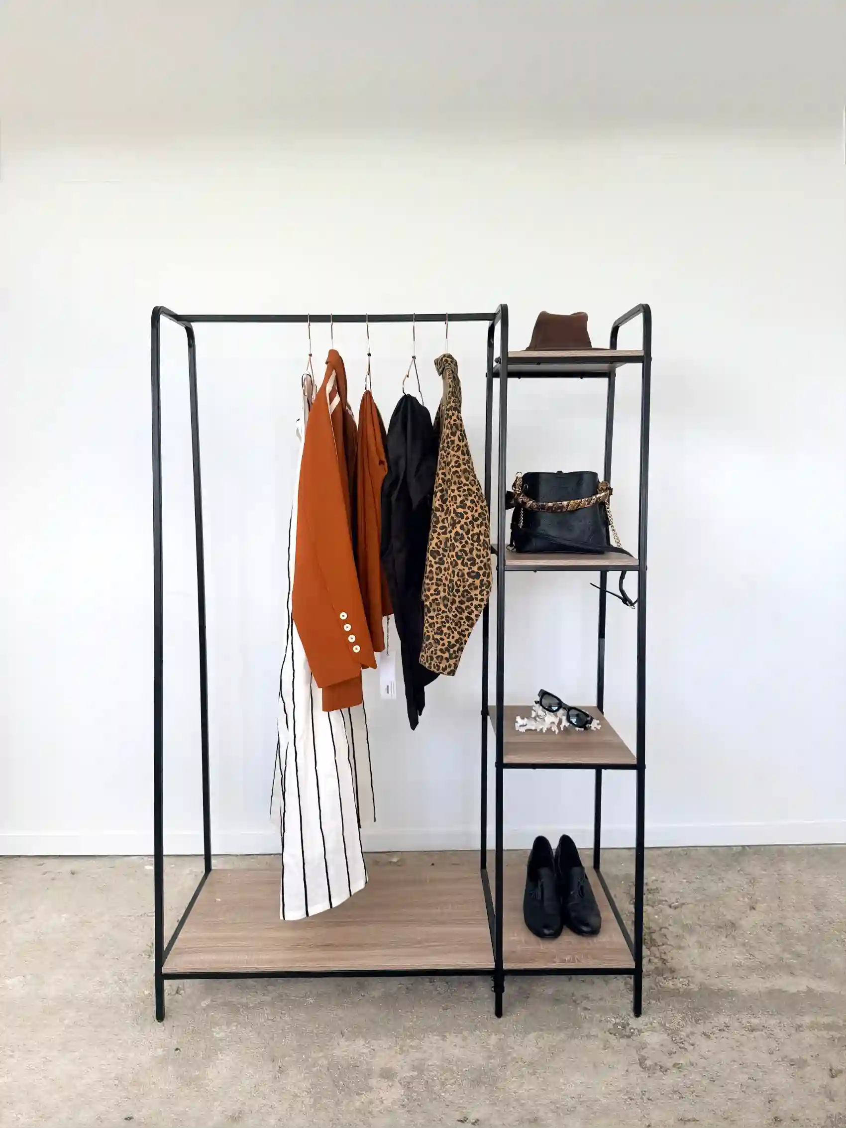 A minimalist clothing rack of neutral-toned wardrobe essentials in cream, camel, and charcoal hanging on wooden hangers.