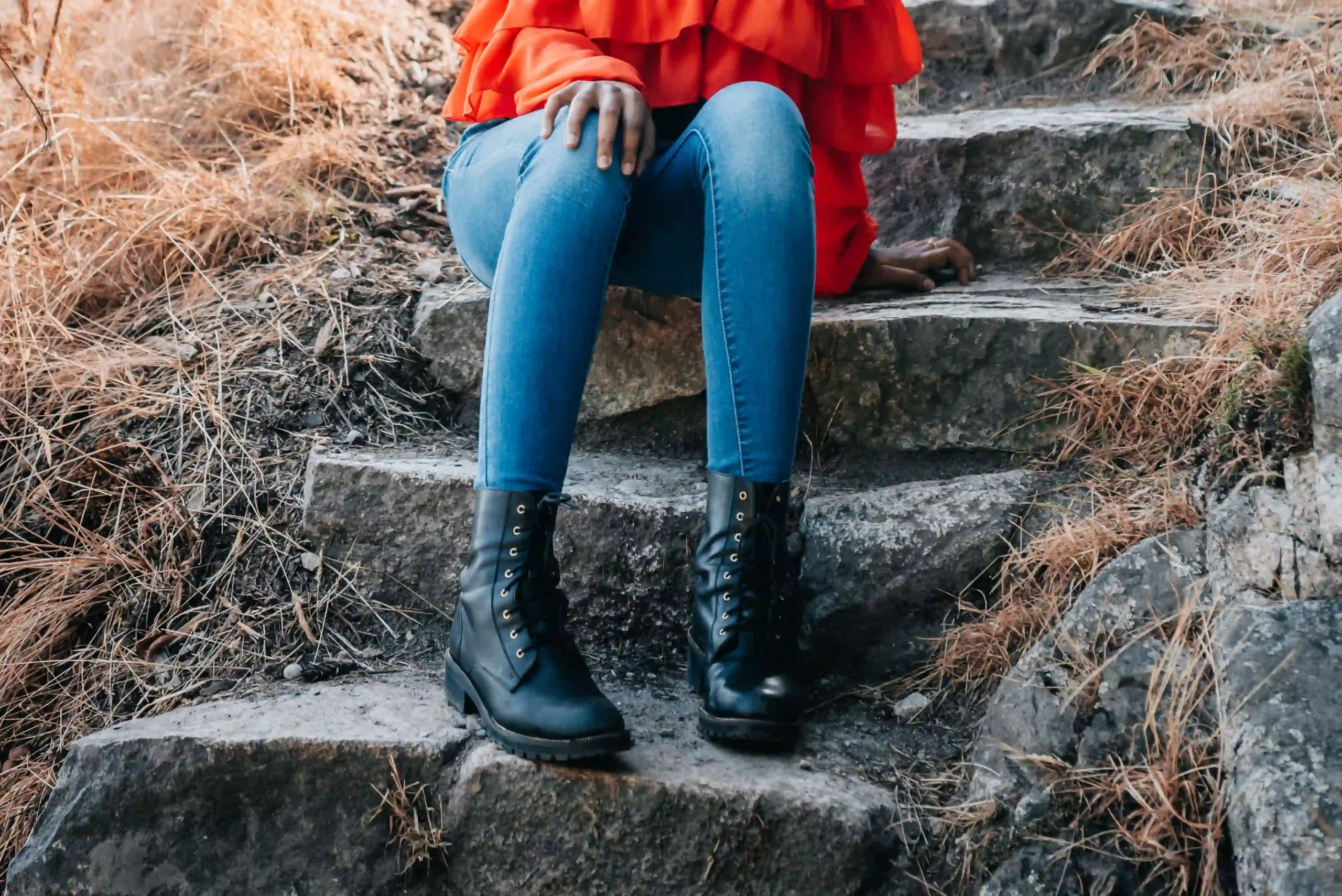Woman in stylish black ankle boots and jeans sitting on outdoor stone steps in an autumn setting