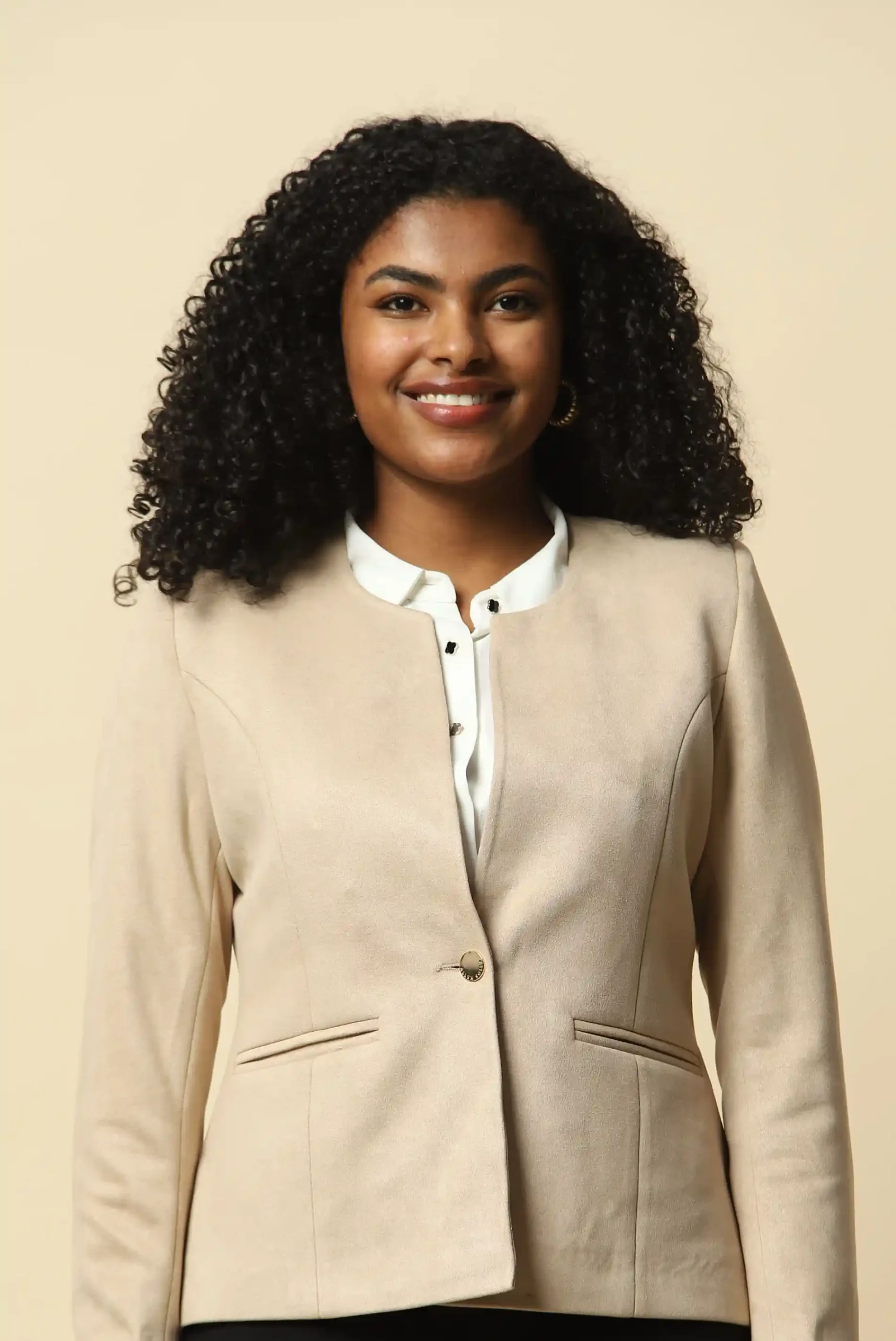 Woman in a beige blazer styled with quiet neutral pieces against a plain background