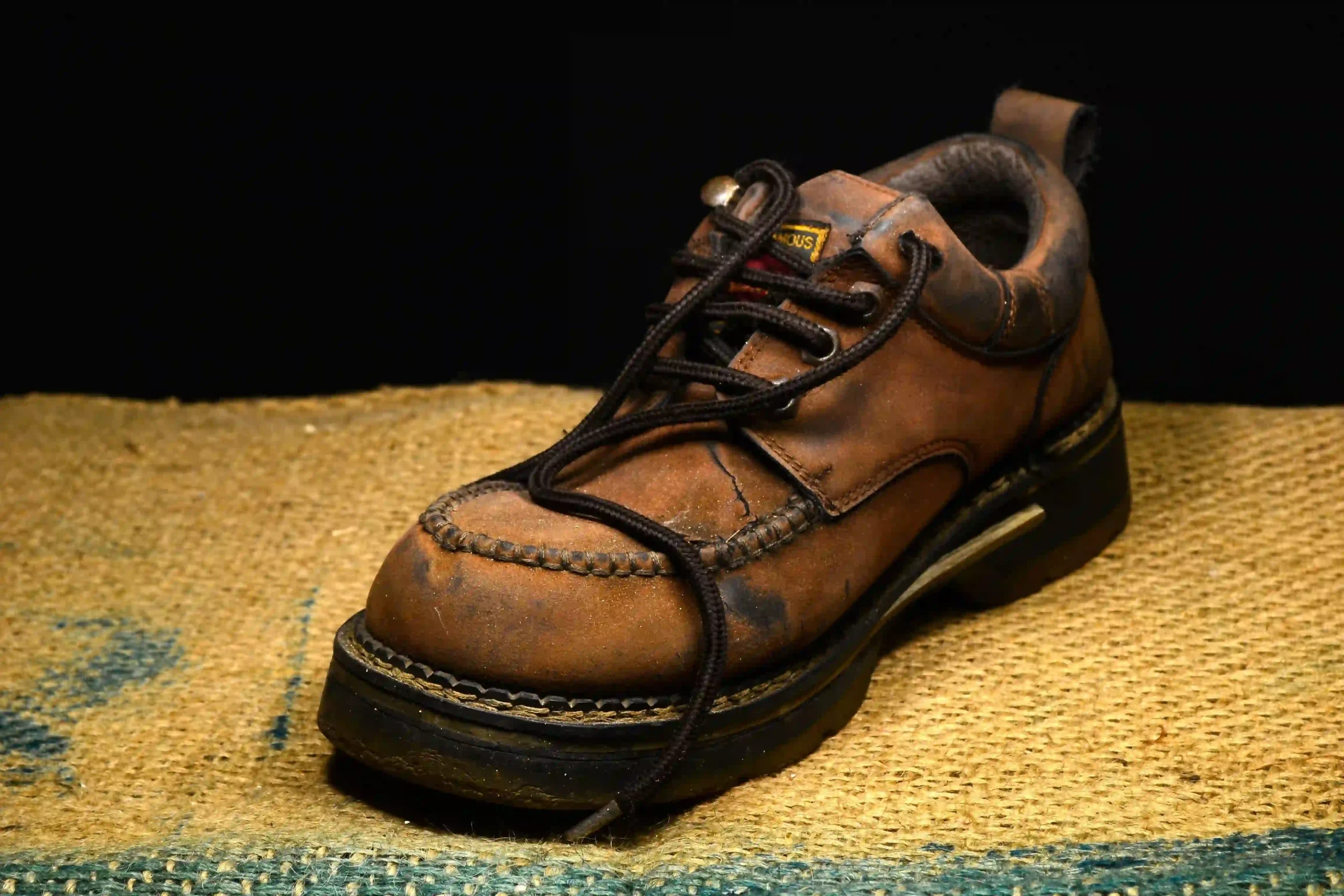 Pair of broken-in brown and black leather work boots photographed on a worn wooden surface