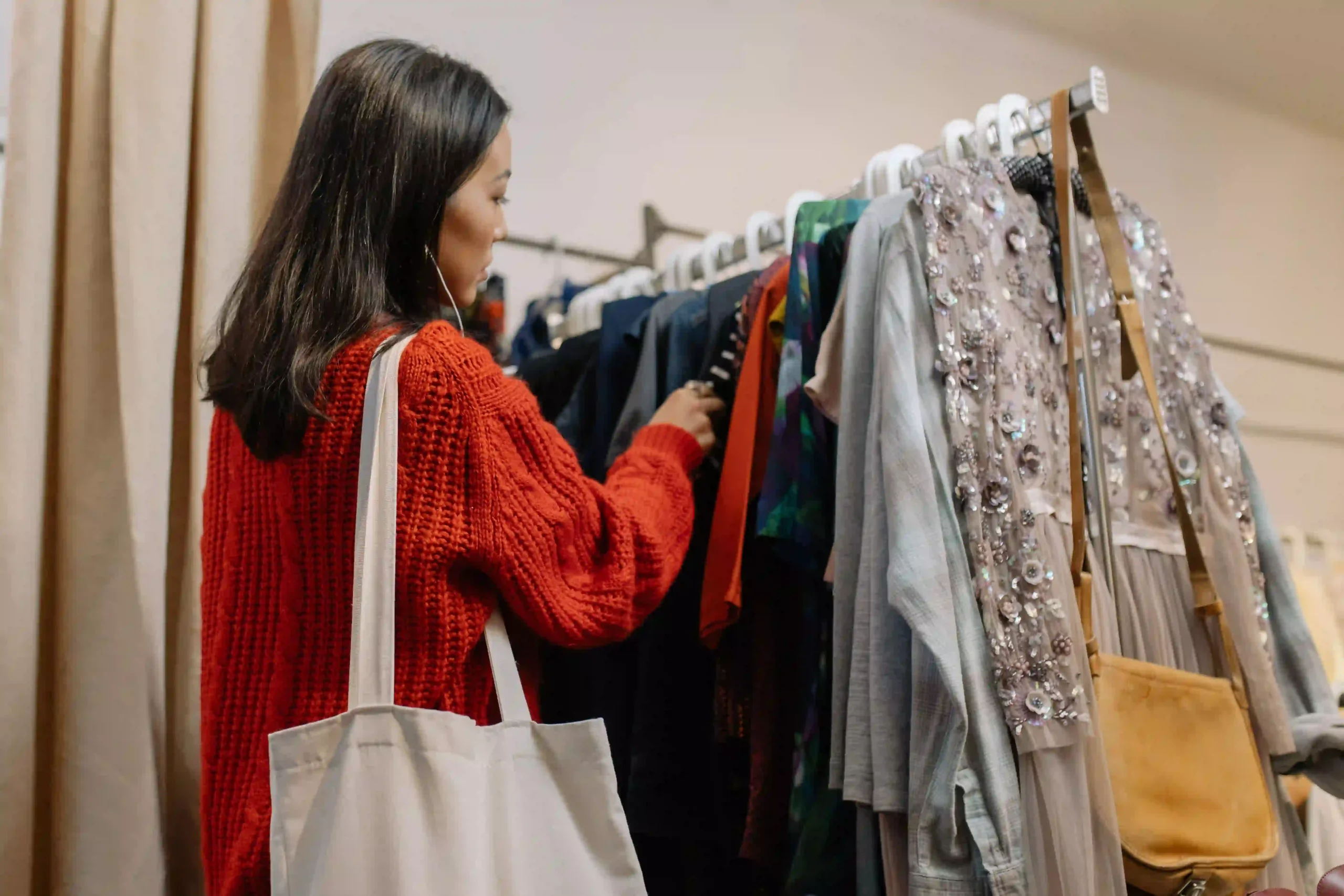 A woman browsing a rack of hanging clothes inside a thrift store