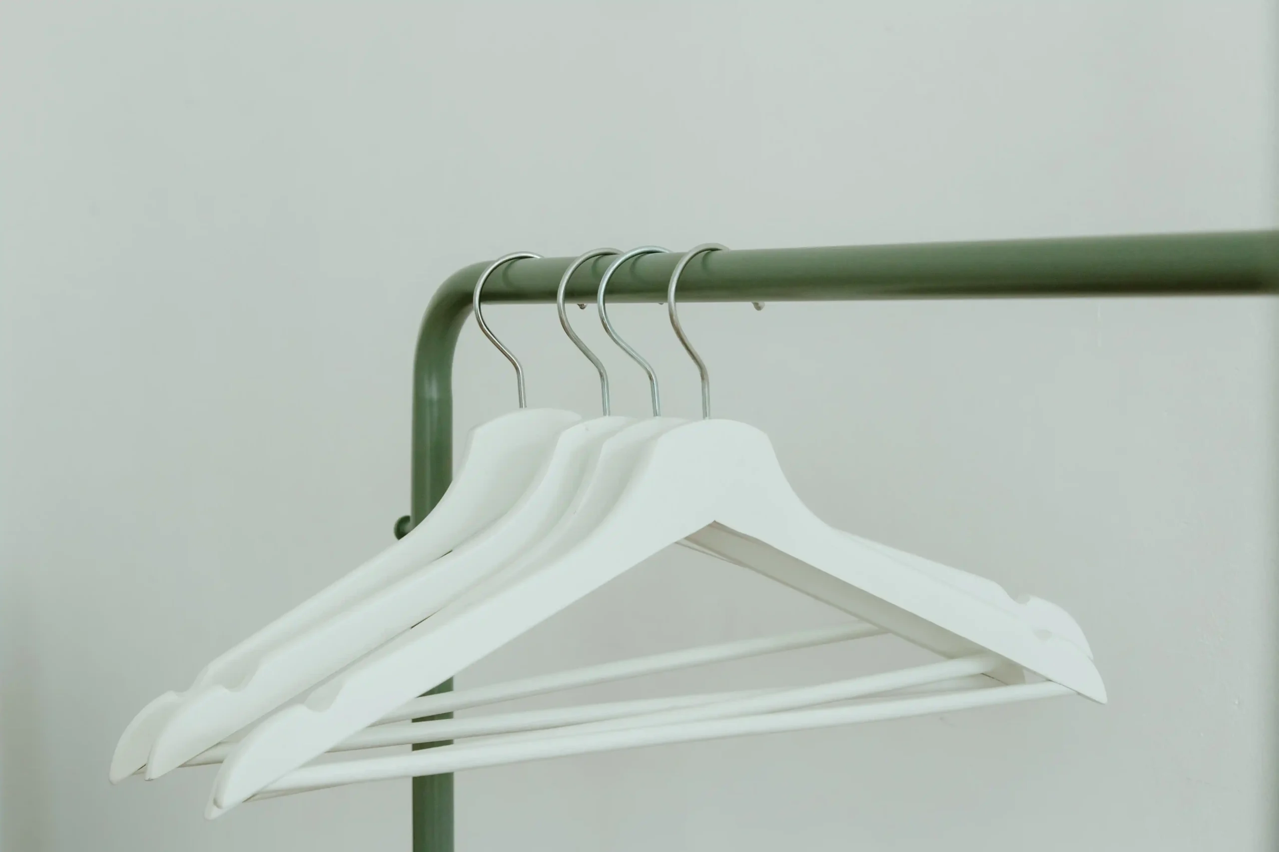 A minimalist clothing rack with neutral garments on white hangers against a plain wall