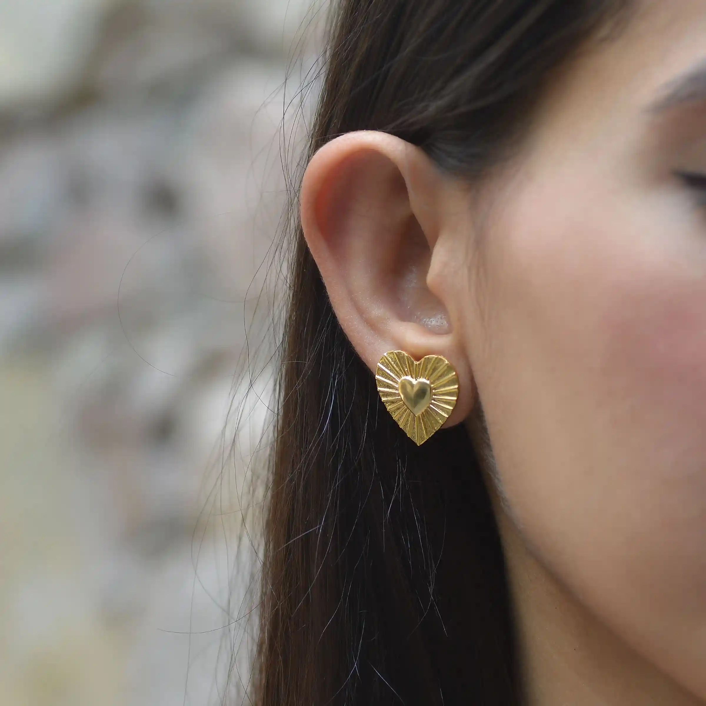 Close-up of a woman's earlobe wearing a small gold earring against soft natural light