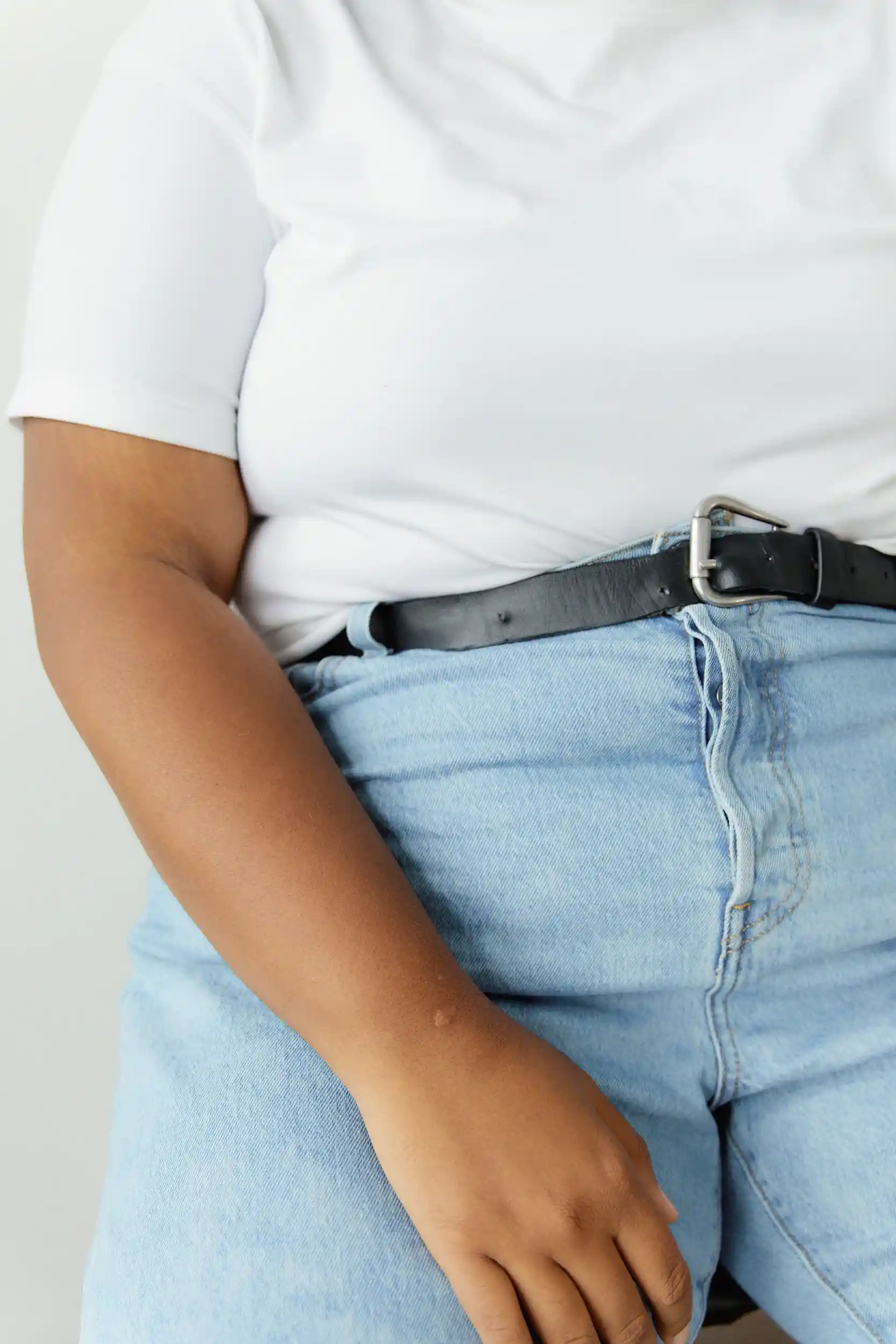 Close view of a plus size woman in a white t-shirt and blue denim jeans showing where the waistband sits on the midsection