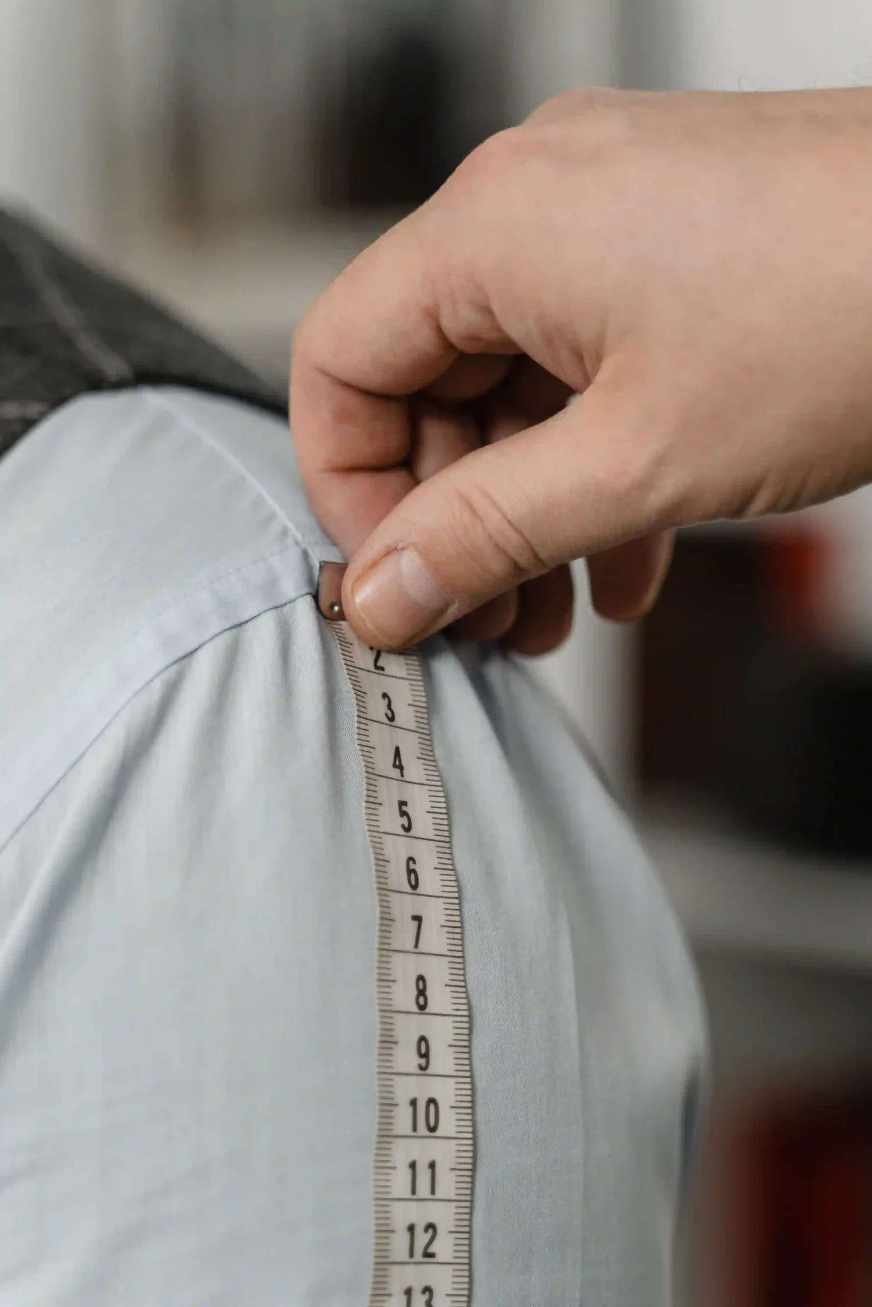 A tailor measuring the sleeve of a garment with a flexible tape measure