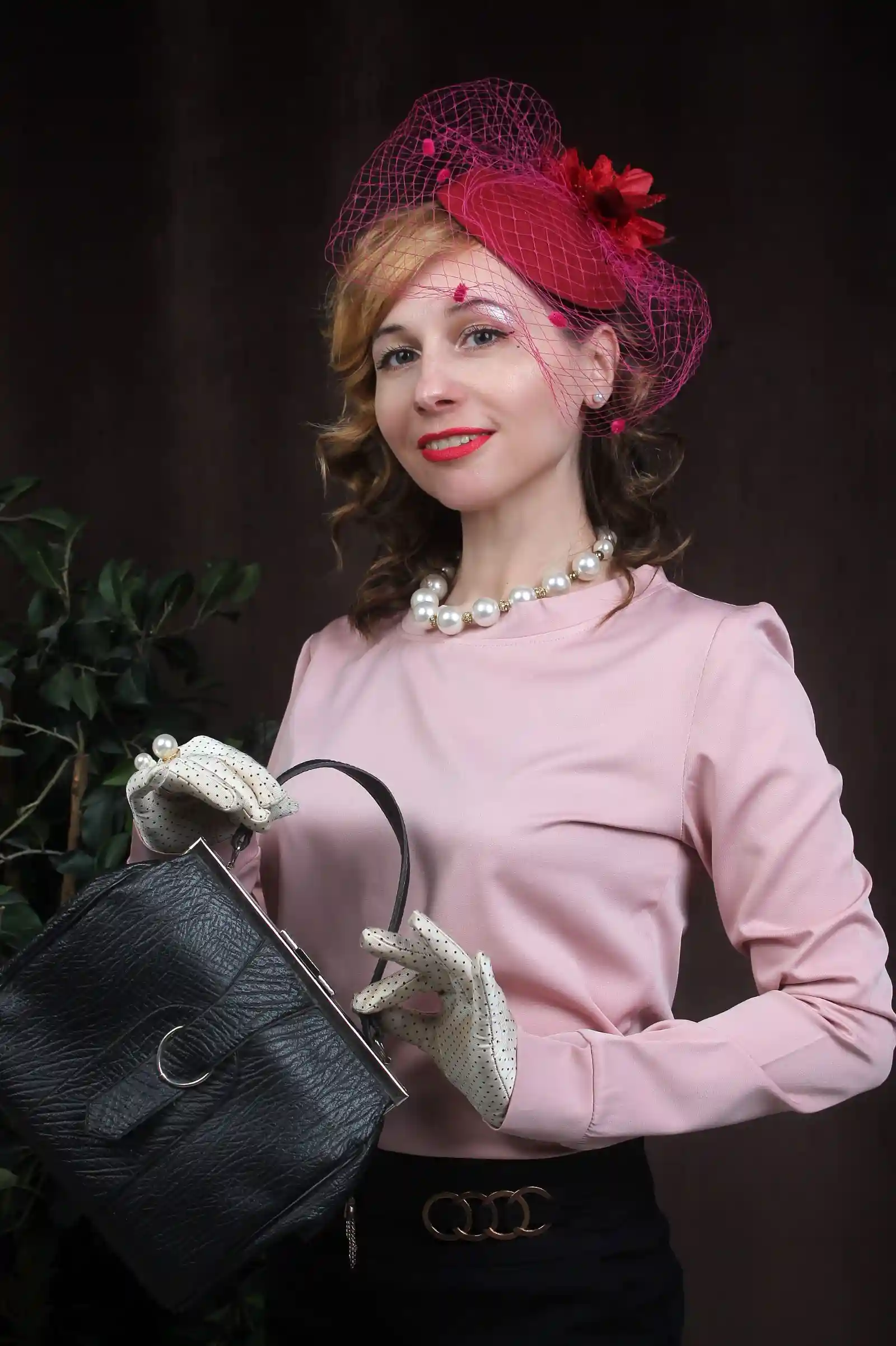 Woman in a pink top wearing a pillbox hat and holding a handbag, showing the hat seated centered on the crown of the head