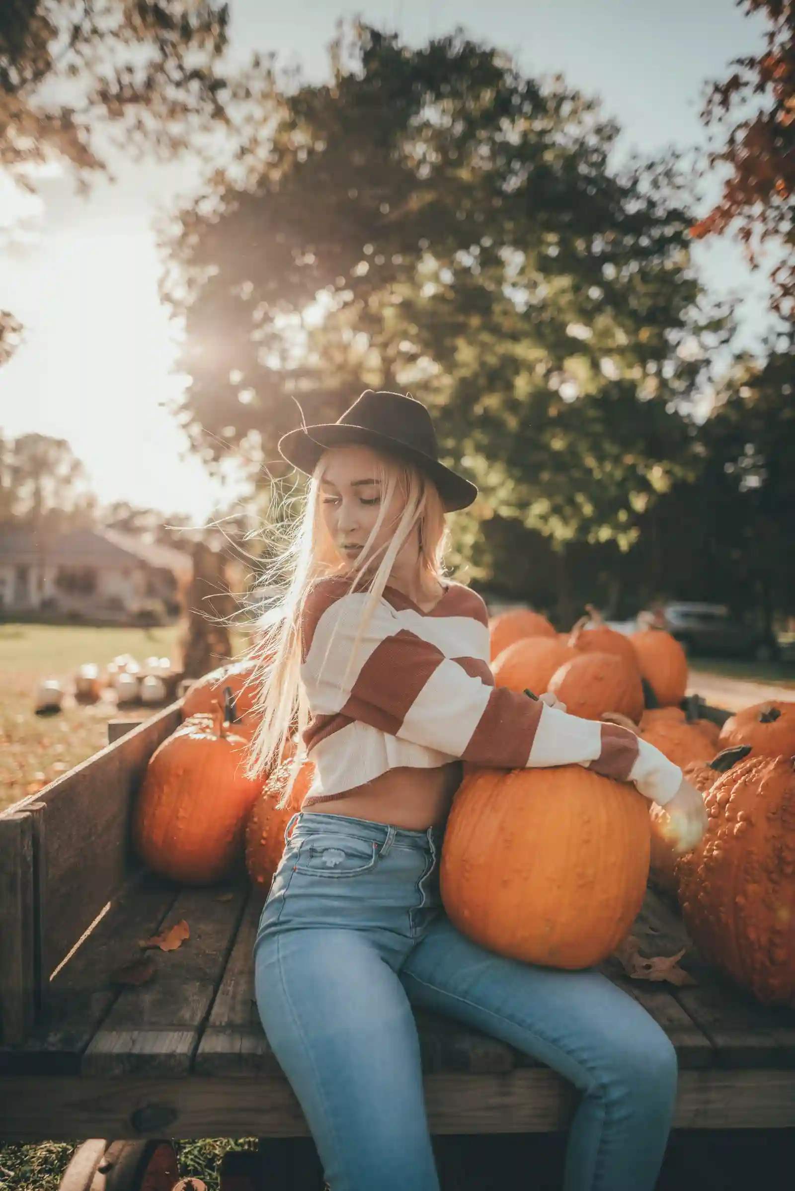 Woman in a cream knit sweater and felt hat sitting on a wagon of pumpkins at a fall farm