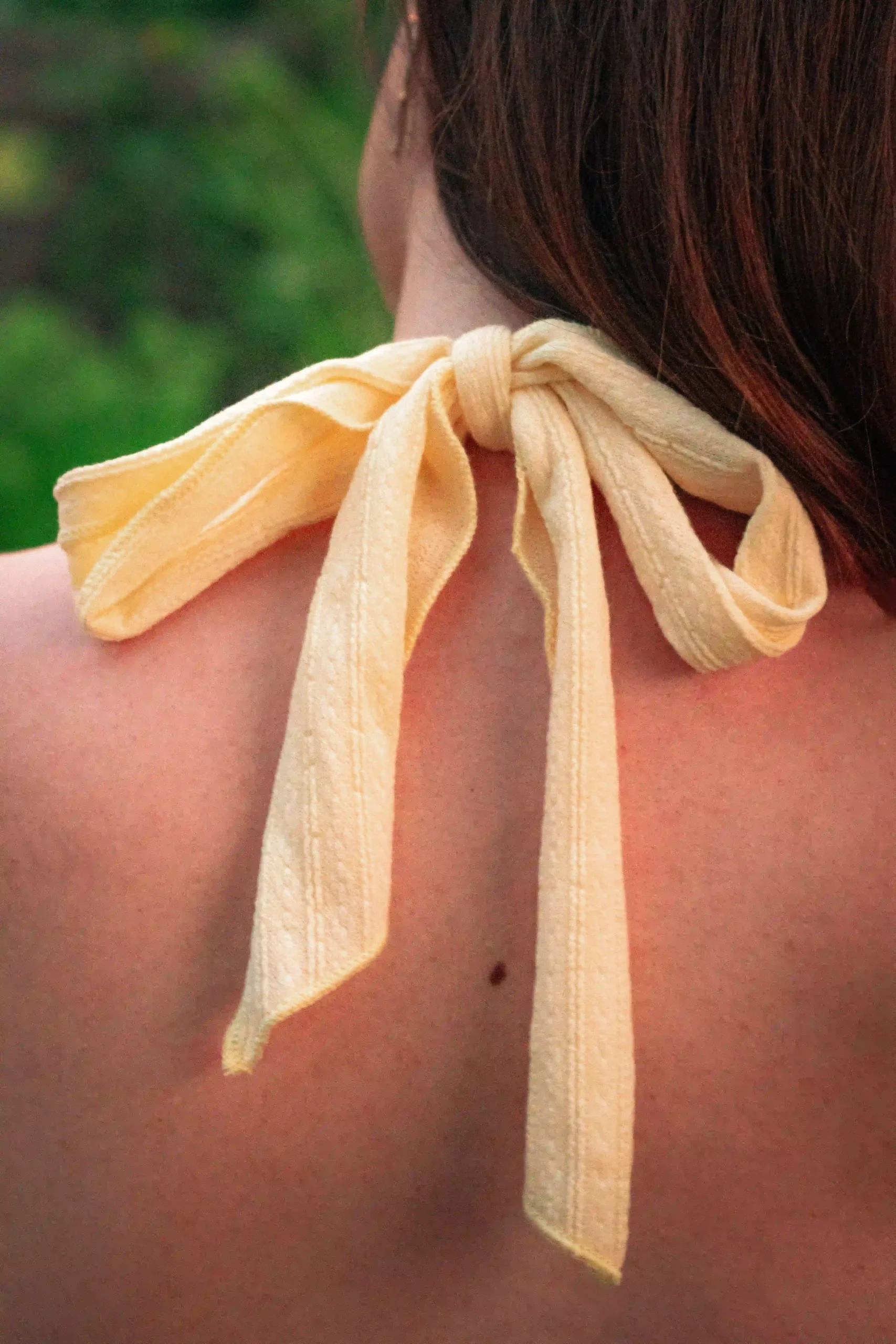 Close-up of a yellow silk scarf tied at a woman's neck outdoors in a summer setting
Caption: none