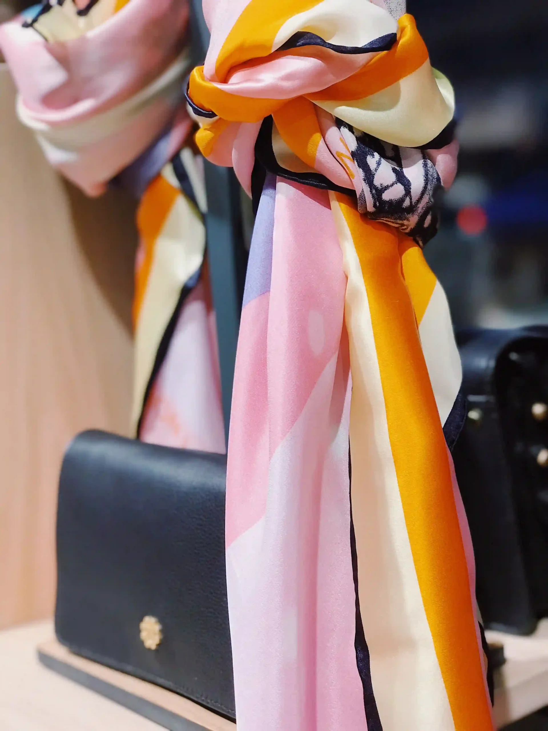 Printed silk scarf draped over the handle of a black leather handbag
Caption: none