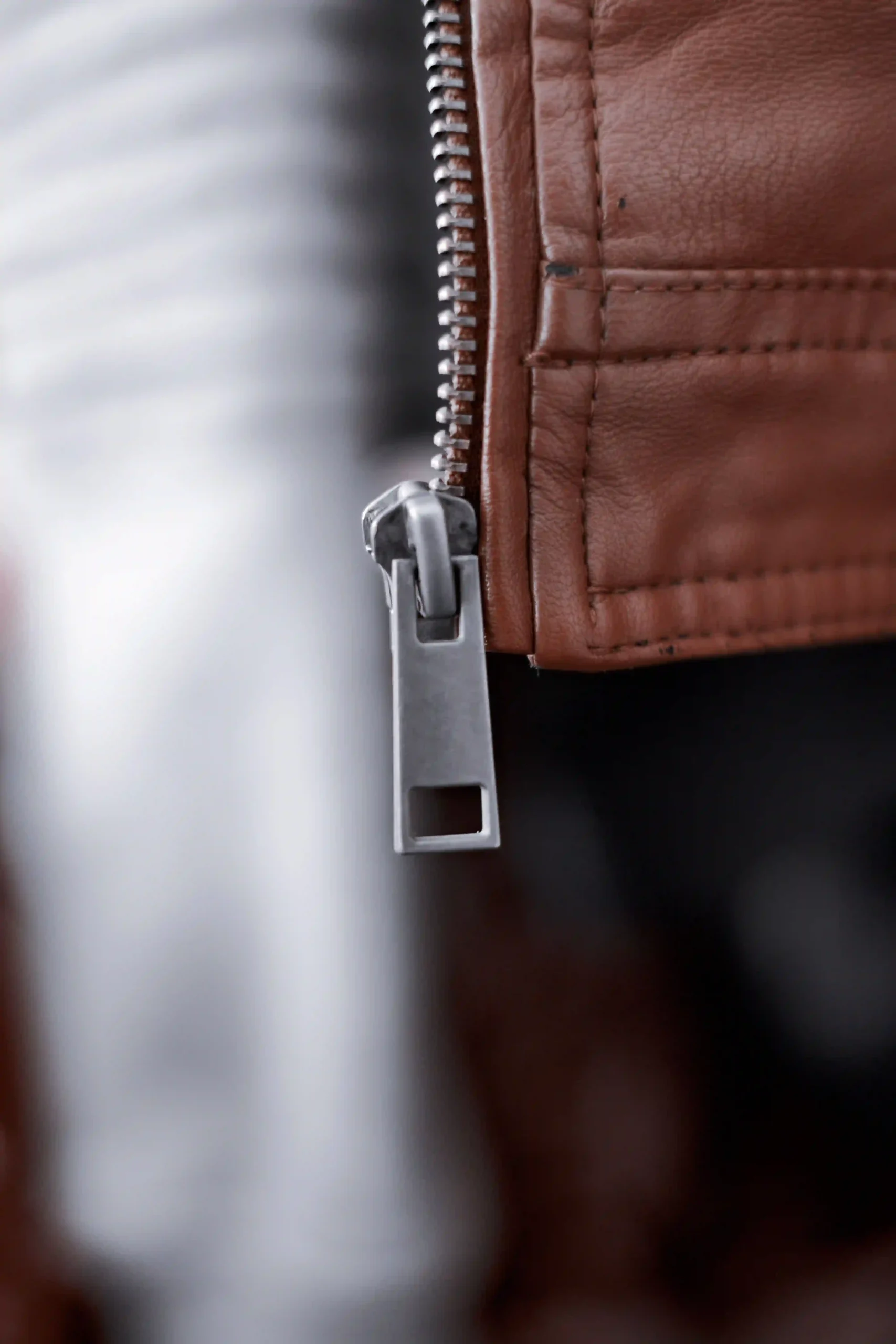 Close-up of a metal zipper and pull on a worn brown leather jacket