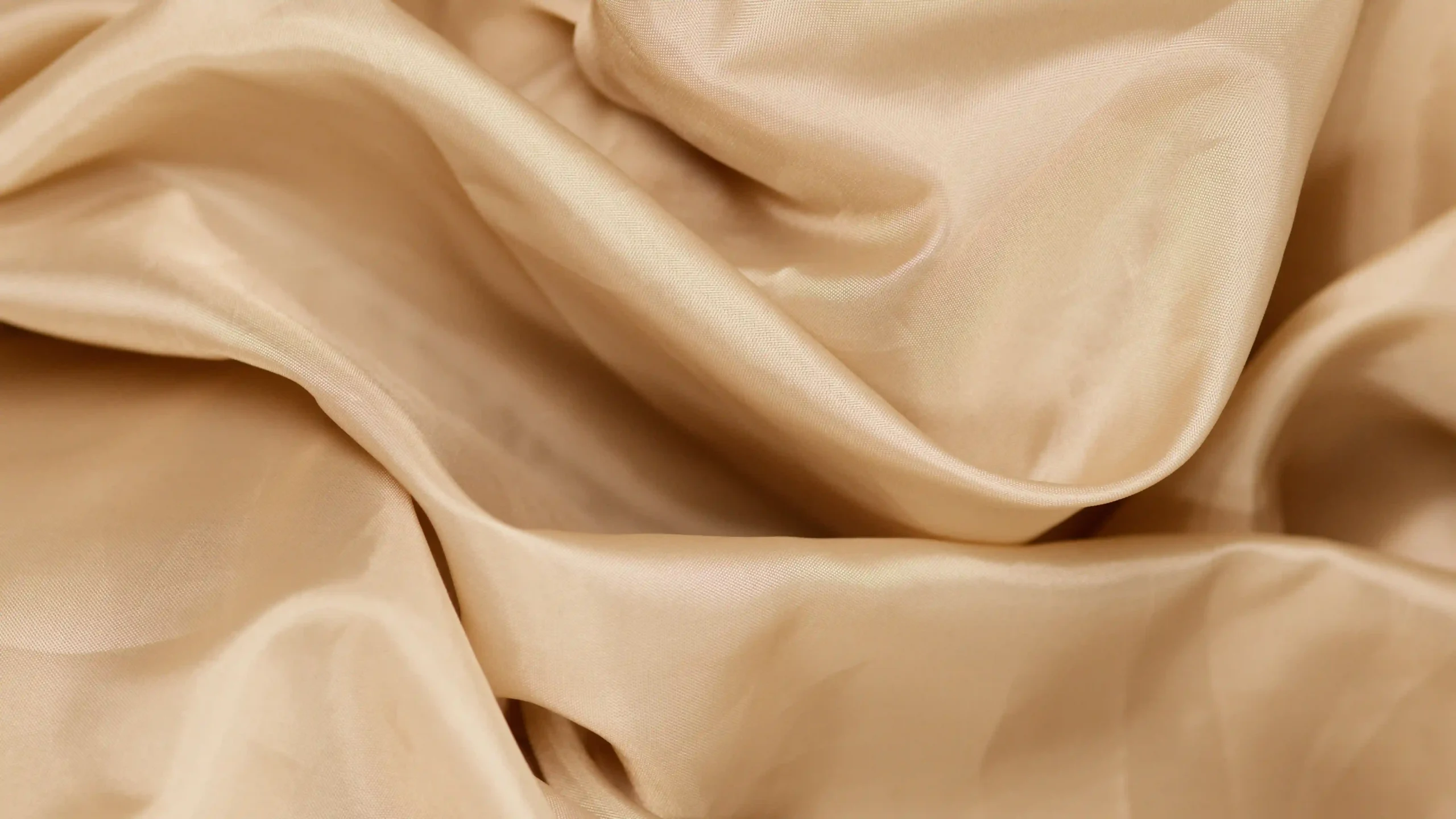 Close-up of beige silk fabric with soft creases and a warm sheen
